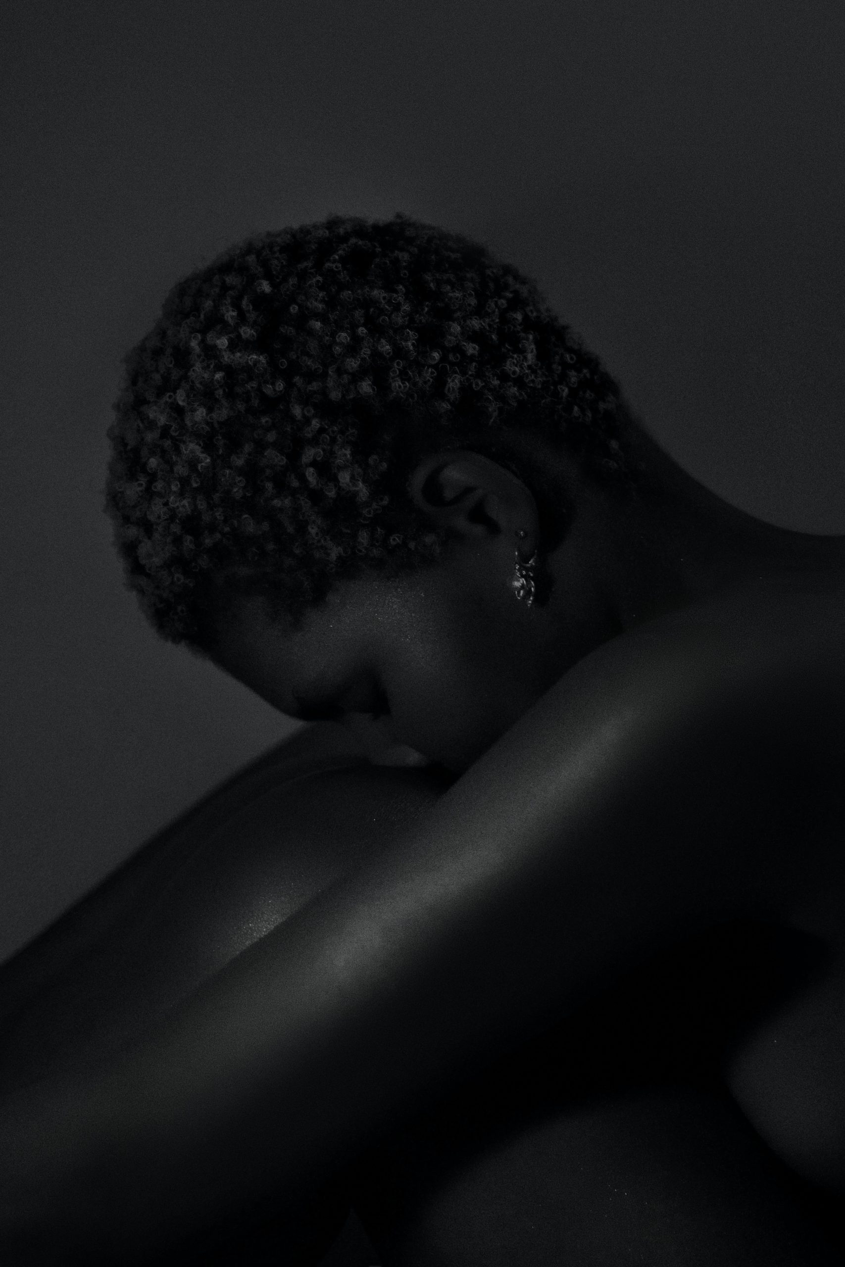 A Black woman with short hair hugs her knees while putting her head on on her knee. A featured image of the blog post Spirituality, The Ancestors, and Systemic Blocks to Success